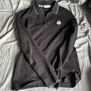 Svart Moncler pikétröja slim fit - Svart långärmad pikétröja från Moncler i slim fit-modell. Moncler-logga på bröstet. Tillverkad i bomull som känns skönt mot huden. Perfekt för en clean och stilren look. Den är 100% äkta då den är köpt på sicuro fasion har äktahets certifikat. Passar dig som har M och även S ny pris ligger på 3900 mitt pris 1300, hör av er vid frågor.