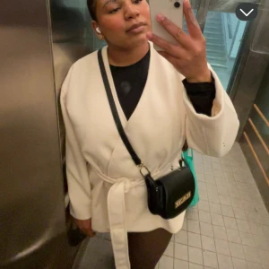 Vit omlott kappa med bälte - Snygg vit omlott kavaj med bälte i midjan som ger en clean och modern look. Jackan har lång ärm och en avslappnad passform, perfekt att styla med jeans eller dressade byxor. Enkel design utan synliga knappar eller dragkedja. Köpt för 500kr i våras.