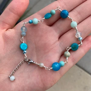 Blått pärlarmband med silverkedja - Unikt armband med blandade blå och turkosa pärlor i olika former och storlekar, trätt på silverfärgad kedja med justerbar längd och karbinlås. Perfekt för dig som gillar färg och vill ha något som sticker ut på handleden.