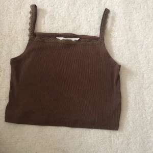 Brun ribbad linnetopp från H&M - Säljer en brun ribbad linnetopp från H&M med smala axelband och fina spetsdetaljer längs banden och halsringen🌸💕 strl: 146/150. Men  det är en ”croptop” så den är ganska kort☺️ använd lite men mycket bra skick. Säljer pga för liten🥰 ‼️pris kan diskuteras‼️