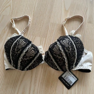 Push-up bh - Helt ny BH från Twilfit, storlek 70B. Elegant modell i svart spets med ljusbeige botten och fina detaljer. Färg: Antique. Aldrig använd, prislappen sitter kvar.