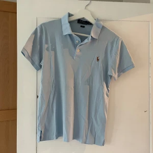 Ljusblå Polo Ralph Lauren t-shirt - Fräsch ljusblå t-shirt från Polo Ralph Lauren i slim fit-modell. Skick 8/10 ungeäfr. Bra i storlek. Lite svett vid armhålorna man det går bort i tvätten mer vannish
