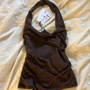 Brun halterneck topp från GinaTricot  - Mörkbrun halterneck topp från GinaTricot. Toppen är helt ny med prislappen kvar, alltså aldrig använd! Säljer då den inte kommit till användning🤎🤎