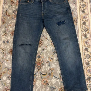 Blåa jeans - Säljer ett par blå jeans med raka ben och slitningar på framsidan. Jeansen är gjorda i robust denim. Rensar garderoben därav säljer jag dem. Hör av er vid intresse 