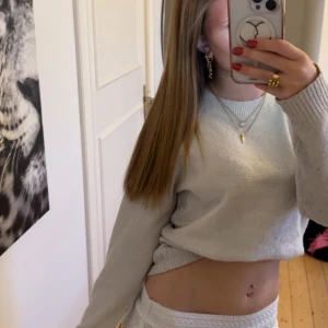 Ljusgrå stickad tröja med rund hals - En enkel och stilren ljusgrå stickad tröja med rund halsringning och ribbade muddar. Tröjan har en normal passform och långa ärmar, perfekt för lager-på-lager under kyligare dagar. Rätt så nopprig