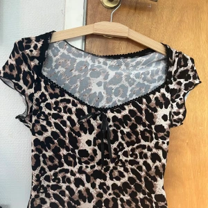 Leopardmönstrad topp från Romwe XS - Säljer en leopardmönstrad topp från Romwe i storlek XS. Toppen har korta ärmar, v-ringning med söt rosettdetalj och svarta spetskanter. Materialet är stretchigt och lätt, perfekt för att sticka ut med ett djurmönster.