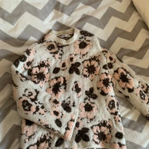 Blommig stickad tröja från Zara - Supermysig stickad tröja från Zara med blommigt mönster i ljusrosa och brunt på en beige bas. Tröjan har rund halsringning och långa ärmar, perfekt för lager på lager. Oversized fit för en chill vibe.