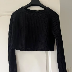 Svart croppad stickad tröja - Säljer en svart croppad stickad tröja med ribbat mönster. Tröjan har rund halsringning och långa ärmar. 
