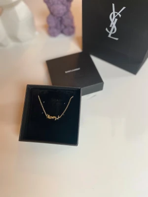 Saint Laurent guldarmband  - Snyggt guldarmband från Saint Laurent med den ikoniska YSL-logotypen i mitten. Kedjan är tunn och elegant med en liten bricka där det står 'Saint Laurent Paris'. Perfekt för dig som gillar lyxiga detaljer och stilren design. Originallåda och originalpåse följer med. Säljer den för 900kr 