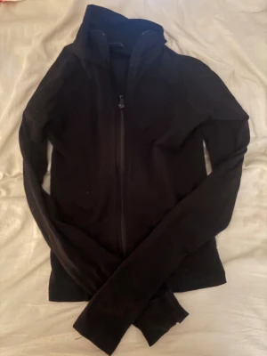 Svart hoodie med dragkedja Gina Tricot - Svart hoodie från Gina Tricot i storlek XS. Modellen har hel dragkedja framtill, lång ärm och en hög krage. Materialet är mjukt och bekvämt, perfekt för chill dagar. Enkel och stilren design utan synliga detaljer eller tryck.