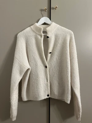 Vit stickad kofta med knappar - Säljer min super fina vit stickad kofta från gestuz med långärmad design och svarta knappar framtill. Storlek xs men sitter som s/m.
