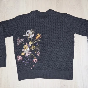 Derschutze "garden of eden" cardigan (S)  - Säljer en mörkgrå stickad kofta från Derschutze i storlek S. Ej använd. Original pris €138. Koftan har ett unikt blommigt broderi på ryggen och mindre broderi framtill, samt knäppning med knappar. Perfekt för dig som gillar detaljer och vill sticka ut. Priset kan negotieras, skicka ett meddelande om ni undrar något!