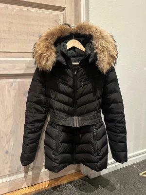 Hollies jacka  - Svart hollies jacka men luva och skärp runt midjan, super fint skick, har några små defekter på baksidan av ärmarna men inget som syns mycket 