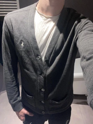 Mörkgrå cardigan från Polo Ralph Lauren - Säljer en galet fet cardigan från ralph lauren i färgen grå. Hade gärna behållit den med har blivit för liten. Den är i storlek M, modellen är 183 och väger ca 73. 👌väldigt bra passform som ni ser på bilden, inga defekter alls🤞