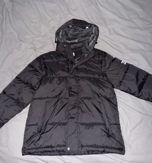 Snygg svart Burberry dunjacka – oanvänd / nytt skick - Säljer denna svarta dunjacka i helt oanvänt skick. Den är varm, lätt och i riktigt bra kvalité. Modellen har dragkedja + knappar framtill, två praktiska sidofickor med dragkedja och en huva med mjukt foder.  Passar perfekt som vinterjacka eller som en lättare övergångsjacka beroende på vad du gillar. Inga defekter, helt som ny.