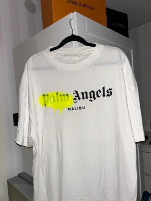 Palm Angels vit t-shirt Malibu XL - Palm Angels t-shirt i vitt med stor svart logotyp och texten 'Malibu' på bröstet. Cool gul spray-effekt över loggan ger en street vibe. Rund hals och korta ärmar. Tillverkad i mjuk 100% bomull för skön känsla. Perfekt för dig som gillar statement-plagg. Nästan helt oanvänd.