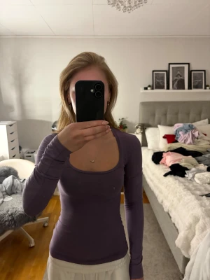 Mörklila långärmad topp från H&M - Säljer en mörklila långärmad topp från H&M med rundad, djup urringning. Modellen är slim och sitter snyggt mot kroppen. Materialet är mjuk bomull som känns skönt mot huden.
