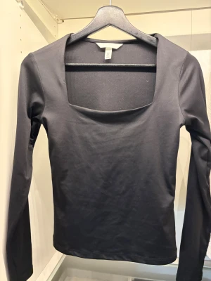 Svart långärmad topp med fyrkantig hals - Svart långärmad topp från H&M med snygg fyrkantig halsringning. Modellen är slim och har en stilren, minimalistisk look. Materialet är mjukt och stretchigt, perfekt för att skapa en clean look