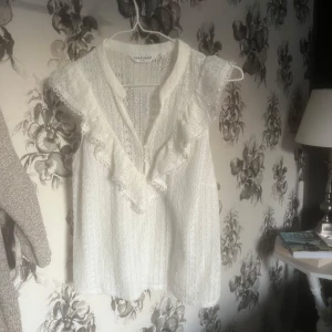 Vit spetsblus från NAFNAF - Säljer en söt vit blus från NAFNAF med spetsdetaljer och volanger. Blusen är ärmlös och har en v-ringad design som ger en romantisk känsla. Perfekt för varmare dagar eller som ett lager under en kavaj. Pris kan diskuteras 💓
