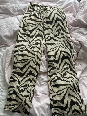 Zebramönstrade linnebyxor från Zara - Snygga linnebyxor från Zara i storlek S med svartvitt zebramönster. Byxorna har en loose passform, elastisk midja med snörning och är tillverkade i ett lätt och luftigt linnematerial. Perfekta för dig som gillar att sticka ut med coola mönster.