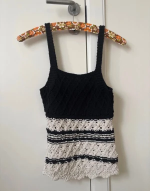 Svart och vit stickad linnetopp - Supersöt stickad linnetopp i svart och vitt med breda axelband. Toppen har ett snyggt mönster med virkade detaljer och vågig nederkant. Perfekt för varma dagar och ger en cool vintagekänsla till din outfit.