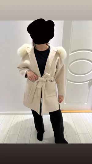 Beige kappa FUR STOCKHOLM - Snygg beige kappa med fluffig äkta päls på kragen och huva. Modellen har knytbälte i midjan och stora fickor framtill. Den är perfekt för dig som gillar stilrena och mysiga plagg. Passar dig i XS/S/. Använt en vinter
