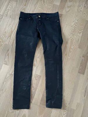 Lågmidjade svarta jeansbyxor från Esprit - Snygga svarta jeansbyxor från Esprit Collection med klassisk femficksdesign och guldfärgade nitar. Byxorna har rak passform och är tillverkade i ett denim-material med lätt glansig finish. Perfekt för dig som gillar stilrena och moderna jeans.