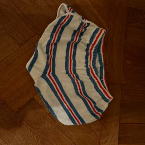 Randiga retro shorts i frotté från we are kids - Säljer ett par vita retro shorts i mjuk frotté med blå och röda ränder. De har elastisk midja och en avslappnad passform, perfekta för sommardagar eller strandhäng.