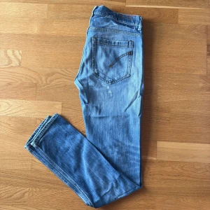 Dondup George - Säljer ett par ljusblå Dondup George jeans med coola slitningar. Jeansen har klassisk femficksdesign, kontrastsömmar och är tillverkade i skönt denimtyg. Perfekt för dig som gillar en avslappnad och trendigstil.