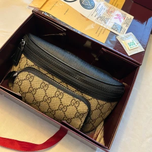 Gucci beige axelväska med GG-mönster - Snygg Gucci axelväska  i beige och svart med klassiskt GG-mönster. Väskan har två fack med dragkedja, svart justerbar rem och detaljer i skinn. Perfekt för dig som vill ha en ikonisk och trendig accessoar med plats för det viktigaste.