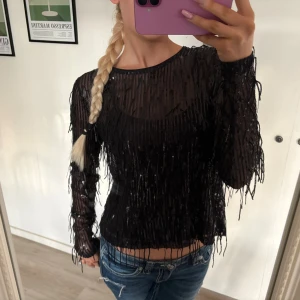 Svart topp med paljetter och fransar - Säljer en svart festtopp från kappahl med långa ärmar, täckt av glittriga paljetter och fransdetaljer. inbyggt linne 💗