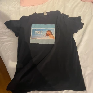 Fin 1989 Taylor Swift tröja 😊💙✨🪩 - Svart t-shirt med tryck framtill som visar Taylor Swifts album 1989 ( taylors version ) 🦋💙köpt på fyndig för ca 2 år sedan men är inte jätteanvänd, är lite smutsig men tror det går bort i tvättmaskinen ⭐️❤️⚡️😊