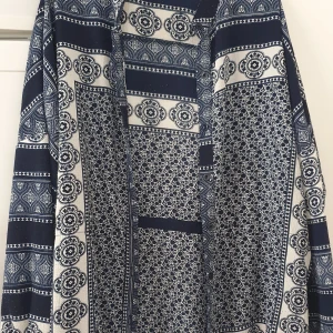 Klänning - Säljer en snygg klänning från Boohoo i blått och vitt med unikt mönster. Klänningen har långa ärmar och ett coolt, nästan boho-inspirerat print med blommiga och geometriska detaljer. Perfekt för dig som vill sticka ut med en statement piece!