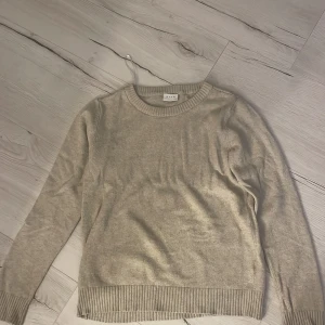 Beige stickad tröja från Vila - Mysig beige stickad tröja från Vila med rund halsringning och ribbade muddar vid ärmslut och nederkant.  Långärmad och i mjukt material som känns skönt mot huden.