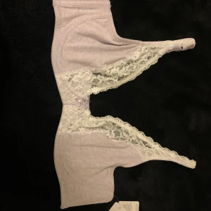 Ljuslila spetsig BH från Cubus - Säljer en ljuslila BH från Cubus med vita spetsdetaljer och en liten rosett framtill. BHn har justerbara axelband och mjukt bomullsmaterial i kombination med dekorativ spets. Perfekt för dig som gillar romantisk och feminin stil.