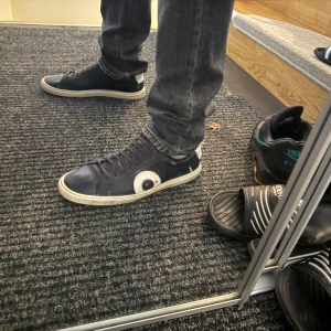 Svarta sneakers från Oliver Cabell - Snygga svarta sneakers från Oliver Cabell med vit detalj på hälen och sidan. Skorna har rund tå, platt sula och snörning. Tillverkade i skinn med en cool kontrast mellan svart och vitt. Perfekta för dig som gillar stilrena och trendiga sneakers. Allt og tillkommer. 