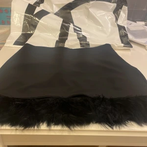 Svart minikjol med fuskpäls från SHEIN  - Supersnygg svart minikjol från Express med fuskpälsdetalj längst ner. Kjolen har en clean och stilren look med rak passform och dragkedja i sidan. Perfekt för dig som vill sticka ut med en trendig twist på klassisk svart kjol.