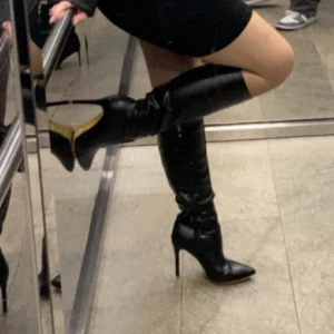 Svarta stövletter med hög klack - Säljer ett par svarta stövletter med spetsig tå och hög klack. Skorna är knähöga och har en elegant, smal siluett som ger en riktigt snygg look. Tillverkade i skinn med en platt sula framtill och klack baktill. Perfekta för att lyfta din outfit. Lite små på mig
