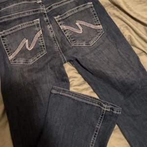 Blå jeans med broderade bakfickor - Snygga blå jeans med klassisk tvätt och vita broderade detaljer på bakfickorna. Jeansen har raka ben och normal passform, perfekta för en avslappnad stil. Lite slitna längst ner på benet