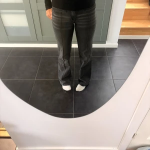 Grå bootcut jeans med broderade fickor - Snygga mörk gråa jeans med bootcut passform och låg midja. Baksidan har broderade fickor med lock och knapp, samt coola detaljer framtill. Jeansen har en lätt tvättad look och dubbla knappar i midjan. Perfekta för dig som gillar unik stil. På bilderna ser färgen lite olika ut men det är endast pågrund av ljuset! Det är lite uttöjda så de kan passa storlek 36