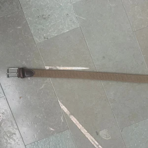 Beige flätat bälte med skinnspänne - Snyggt beige bälte med flätad design och detaljer i mörkbrunt skinn vid spännet. Spännet är i silverfärgad metall och ger en stilren touch. Perfekt för att lyfta din outfit med en klassisk och tidlös accessoar. Köpt för 1000