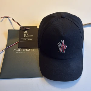 Moncler Grenoble keps - Snygg svart keps från Moncler Grenoble med broderad logga i rött, vitt och blått framtill. Klassisk böjd skärm och justerbar passform. Tillverkad i bomull för en bekväm känsla. Köpt för 3000 på Care of Carl, knappt använt då den inte passa mig. Pris kan diskuteras !😁