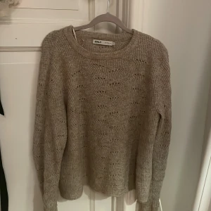 Beige stickad tröja från ONLY - Mysig beige stickad tröja från ONLY med rund halsringning och diskret mönsterstickning. Tröjan har lång ärm och en avslappnad passform, perfekt för kyliga dagar. Enkel att matcha med jeans eller kjol. Skriv för fler frågor och bilder!