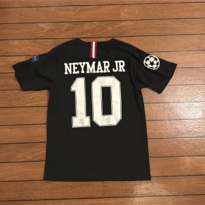 PSG Neymar Jr svart matchtröja - Svart PSG fotbollströja med Neymar Jr och nummer 10 på ryggen. Jordan-logga och Paris Saint-Germain-emblem på bröstet, samt Fly Emirates-tryck. Kortärmad med Champions League-märke på ärmen. Tillverkad i lätt polyester, exklusiv produkt.