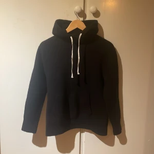 Svart hoodie från AllSaints med huva - Svart hoodie från AllSaints i storlek small. Klassisk modell i ull med vit snörning i huvan och känguruficka framtill. Mjuk och skön, perfekt för chill dagar. Långärmad och enkel design som funkar till det mesta.