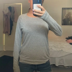 Grå långärmad tröja från Lindex - En enkel och skön grå långärmad tröja från Lindex i storlek S. Tröjan har rund hals och är tillverkad i mjukt bomullsmaterial med melerad look. Perfekt att slänga på sig till jeans eller shorts för en chill stil.