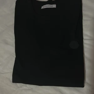 Svart Moncler t-shirt med logga - Snygg svart t-shirt från Moncler med rund hals och diskret svart logopatch på bröstet. Klassisk och stilren design som funkar till allt. Mjuk bomullskvalitet och korta ärmar för en clean look.