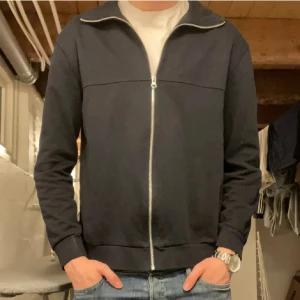 Svart ziptröja från East West - Svart ziptröja från East West i klassisk modell med hel dragkedja framtill och ståkrage. Tröjan har långa ärmar och ribbade muddar vid ärmslut och nederkant. Perfekt till jeans eller över en t-shirt för en clean look.