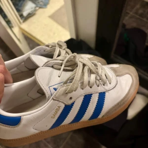 Adidas Samba vit/blå sneakers - Klassiska Adidas Samba sneakers i vitt skinn med blå ränder. Säljer dom då jag inte känner att de passar mig🤗