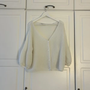 Vit stickad kofta från NA-KD💕💕 - Mysig vit stickad kofta från NA-KD med v-ringning och fyra knappar framtill. Koftan har ballongärmar och är lite croppad i modellen. Perfekt för lager-på-lager och har en mjuk, fluffig känsla. Passar dig som gillar enkel och stilren look.